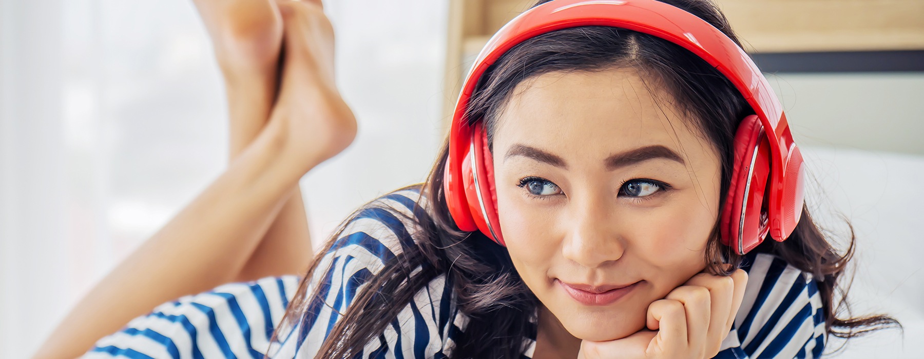 lifestyle image of a young woman listening to music through over-the-ear headphones